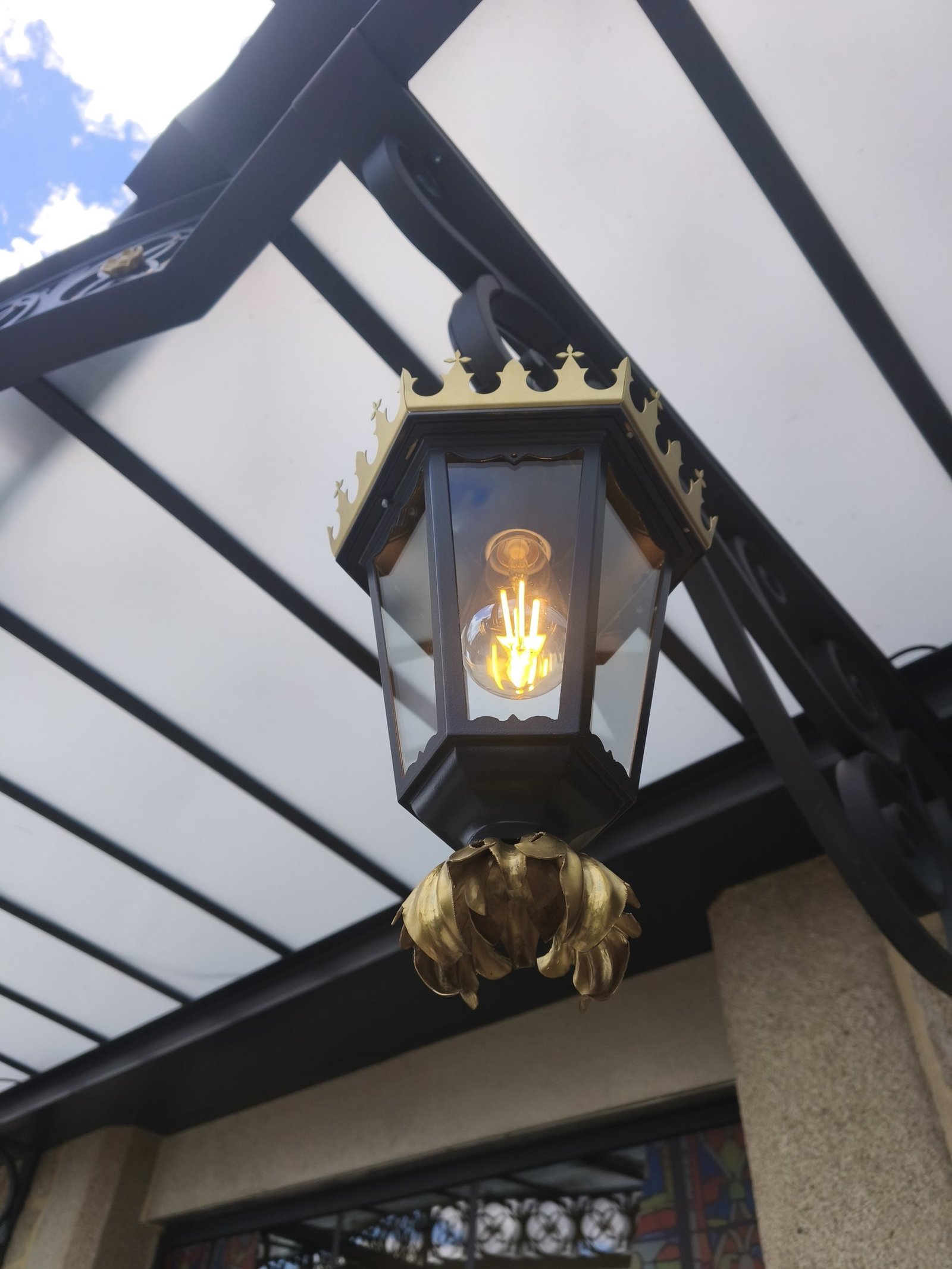 Lanterne ornée d’une fleur en laiton repoussé sous une marquise en ferronnerie d’art